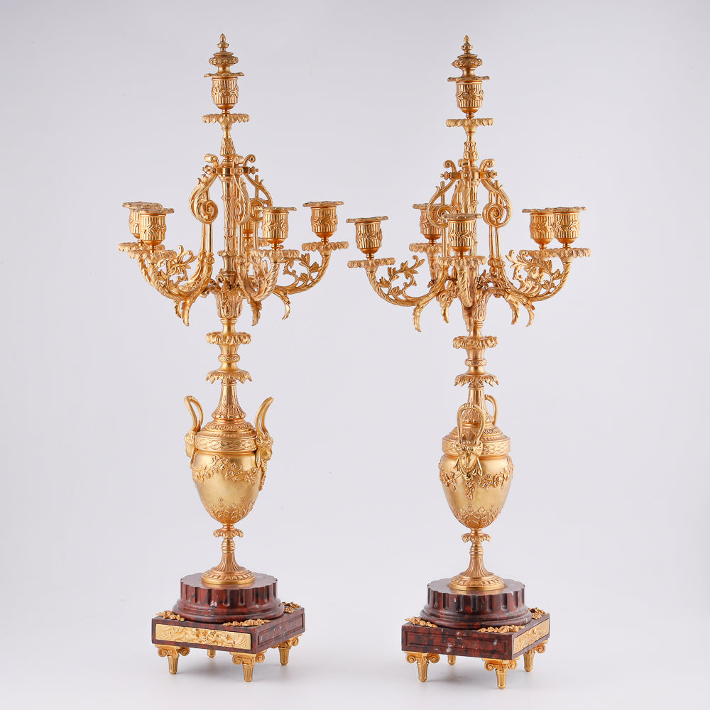 Pareja de candelabros antiguos sobre pedestal de mármol.