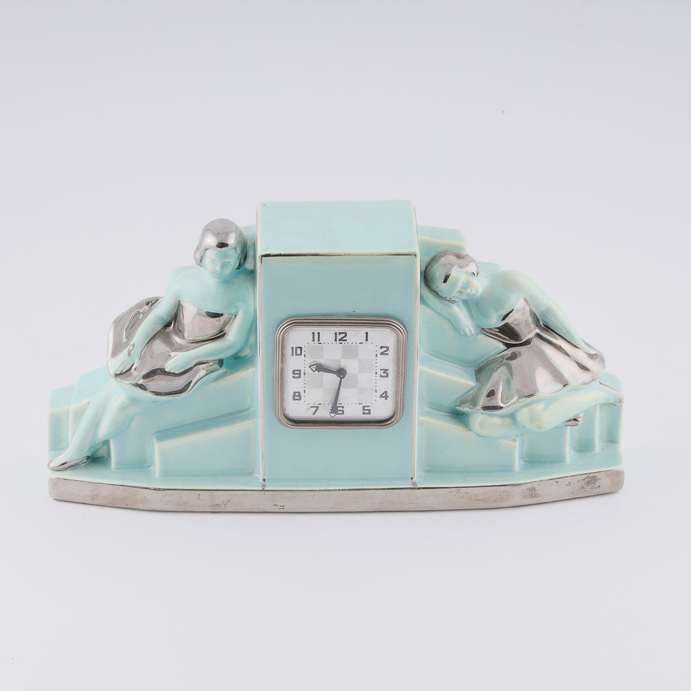 Reloj Fajance Art Deco con forma de pedestal y dos elegantes bailarinas sentadas con gracia a cada lado.