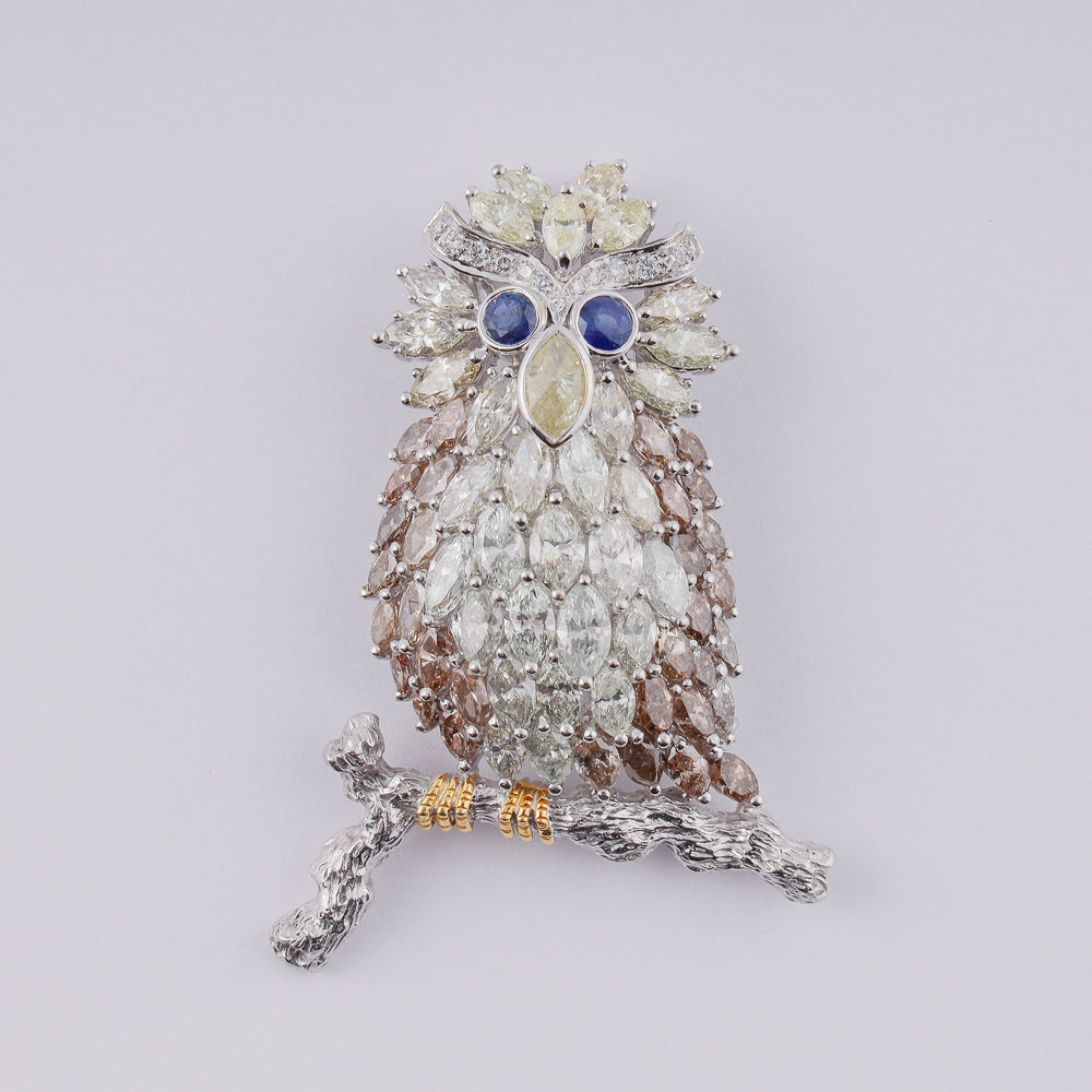 18k white gold brooch designed as an owl on a branch set with 14,18 CTW of diamonds and 2 blue sapphires