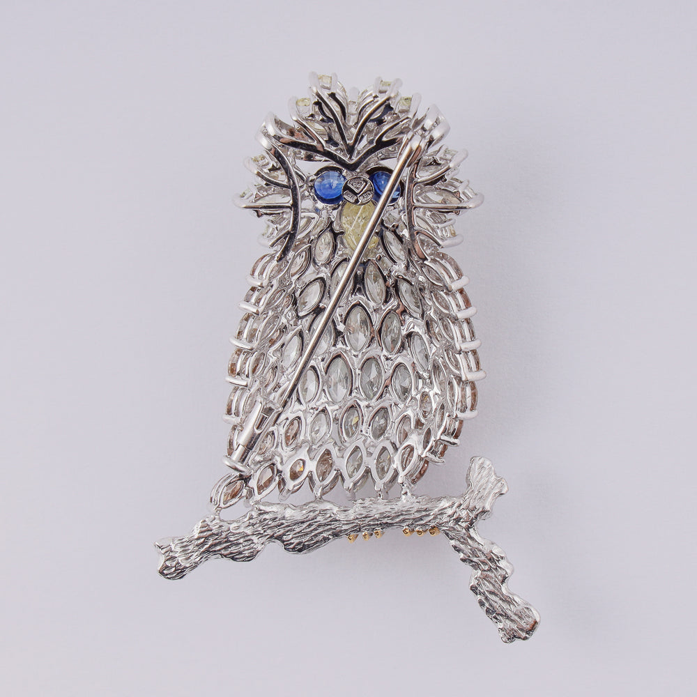 18k white gold brooch designed as an owl on a branch set with 14,18 CTW of diamonds and 2 blue sapphires