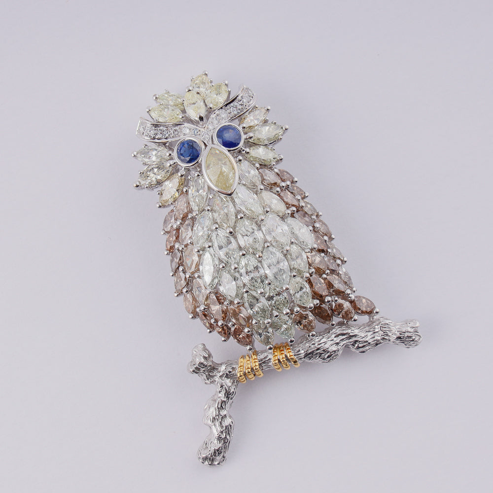 18k white gold brooch designed as an owl on a branch set with 14,18 CTW of diamonds and 2 blue sapphires